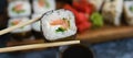 Hand holds wooden sticks sushi roll with spinach, cheese, salmon and nori. Large set of rolls on the background Royalty Free Stock Photo