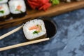 Hand holds wooden sticks sushi roll with spinach, cheese, salmon and nori. Large set of rolls on the background Royalty Free Stock Photo