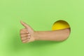 Hand through hole in green background keeps thumb up, demonstrates approval sign showing like gesture