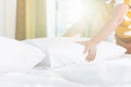 Hand of housekeeper set up white pillow on the bed sheet in hotel room at morning time with sunlight from windows Royalty Free Stock Photo