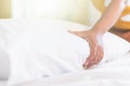 Hand of housekeeper set up white pillow on the bed sheet in hotel room at morning time with sunlight from windows Royalty Free Stock Photo