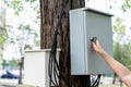 Hand of human electrician opens or closes electrical box on trunk of tree in park