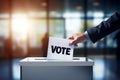 Hand inserting a & x27;VOTE& x27; labeled ballot into a slot of a polling box, office setting with sunlight Royalty Free Stock Photo