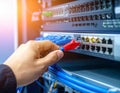 Hand plugging a red ethernet cable into a network switch in a server rack with blue cables and warm light Keywords Royalty Free Stock Photo