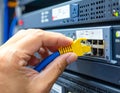 Hand plugging a yellow ethernet cable into a network switch in a server rack with blue cables and soft lighting Royalty Free Stock Photo