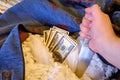 A hand with a knife rips open the lining of an old sofa and takes out dollars banknotes. Stealing money hidden at home in a pillow Royalty Free Stock Photo