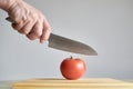 Hand with a knife, about to cut a ripe tomato on a wooden chopping board Royalty Free Stock Photo