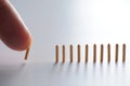 Hand Knocking Down Miniature Light Brown Columns Set Against Light Background. Visualizing Domino Effect, Sequence of Events Royalty Free Stock Photo
