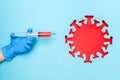 Hand in latex glove hold syringe with vaccine drug and abstract red coronavirus, virus, bacteria, microbe, blue background.