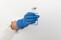 Hand in a latex glove holding a medical glass bottle through torn white wall