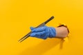 Hand in a latex glove holding medical tweezers through torn yellow wall Royalty Free Stock Photo
