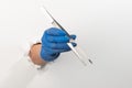 Hand in a latex glove holding tweezers through torn white wall Royalty Free Stock Photo