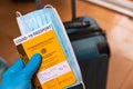 Hand with latex gloves holding covid vaccine passport and face mask concept with luggage at airport. traveling and tourism during