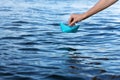 Hand launches a blue paper boat into clear water