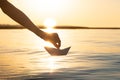 The hand launches the paper ship into the water. Beautiful summer sunset on the river and origami paper boat