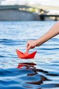 Hand launches a red paper boat into clear water, paper ship in hand, dream of freedom, travel and adventure