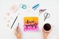 Hand lettered motivation sign Love Yourself, watercolors, brushes, woman`s hand holding cup of tea and other stationary supplies