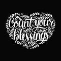 Hand lettering with quotes Count your blessing with leaves in shape of heart on black background.