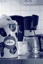 A hand lies on top of a coffee tin can, a cup and a coffee machine is seen in the background Royalty Free Stock Photo