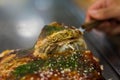 Hand lifting a slice of Hiroshima style Okonomiyaki with a spatula. Japanese style layered pancake filled with shredded cabbage