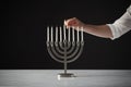 Hand Lighting Candle On Metal Hanukkah Menorah On Marble Surface Against Black Studio Background