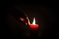 A hand lighting a red candle in the darkness