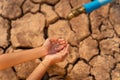 Hand of little girl wating for a drip of water from a faucet at dry ground. Water scarcity and crisis concept