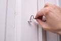 A hand locking a door hook on white wooden door, simple device for home house safety and protection