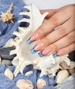 Hand with long artificial blue french manicured nails holding a seashell