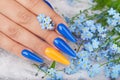 Hand with long artificial manicured nails colored with blue and orange nail polish