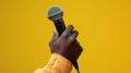 Hand Holding a Microphone Against Yellow.AI generated image Royalty Free Stock Photo