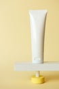 Hand lotion white tube standing on abstract pedestal on pastel yellow background with copy space, front view. Blank cosmetic