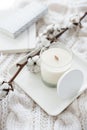 Hand-made candle with cotton branch on white cozy winter blanket