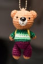 Hand made key ring brown teddy bear knitted doll wearing a green and white shirt and violet plant Royalty Free Stock Photo