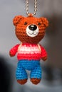 Hand made key ring brown teddy bear knitted doll wearing a red and white shirt and blue plant Royalty Free Stock Photo