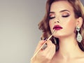 Hand of make-up master is painting lips of young beautiful brunette model. Royalty Free Stock Photo