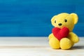 Hand make yarn red heart put on yellow teddy bear in front of white pot and green ornamental plants on wooden table and blue backg Royalty Free Stock Photo