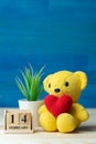 Hand make yarn red heart put on yellow teddy bear beside wooden block calendar set on Valentines date 14 February in front of Royalty Free Stock Photo