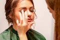 The hand of a makeup artist applies eye shadow on the eyelid of a young Caucasian woman with fingers in a beauty salon.