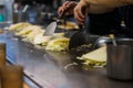 Hand making a Japanese Hiroshima style layered pancake, Okonomiyaki, on a hot pan