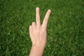 Hand making victory sign on green grass background Royalty Free Stock Photo