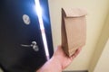 The hand of a male courier holds an eco friendly paper bag at the door. Express delivery to the door of the apartment.