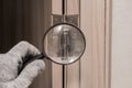 The hand of a male worker in a construction glove examines through a magnifying glass the door hinge of a wooden door. The concept