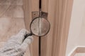 The hand of a male worker in a construction glove examines through a magnifying glass the door hinge of a wooden door. The concept