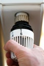 Hand of man adjusting radiator thermostat valve to number 5 icon, symbol for high heating costs or warm temperature setting