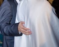 Hand of a man in black jacket hugs bride in white. View from the back