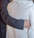 Hand of a man in black jacket hugs bride in white. View from the back