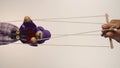 The hand of a man controls a clown marionette hanging on strings. A rag doll in a purple suit and hat, with a red bow Royalty Free Stock Photo