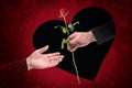 Hand of a man is giving a rose through a heart shaped black hole in a red greeting card to the hand of a woman on Valentines day,