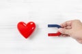 Hand of Man hold Magnet attracting Red Heart on white wood background. Love Concept with Copy Space